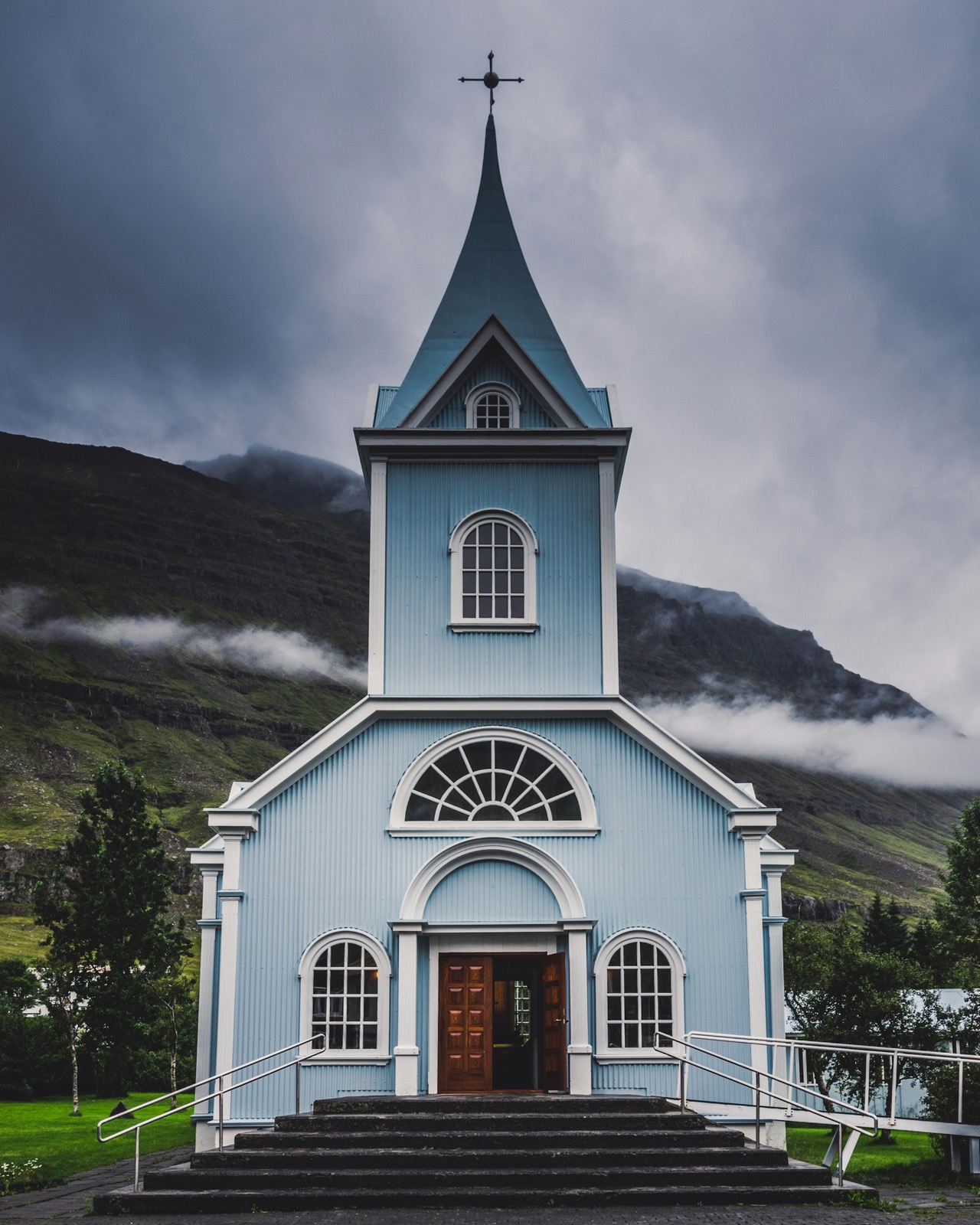 Seyðisfjarðarkirkja, the blue church at Seyðisfjörður, under low storm cloud with the fjord wall behind it