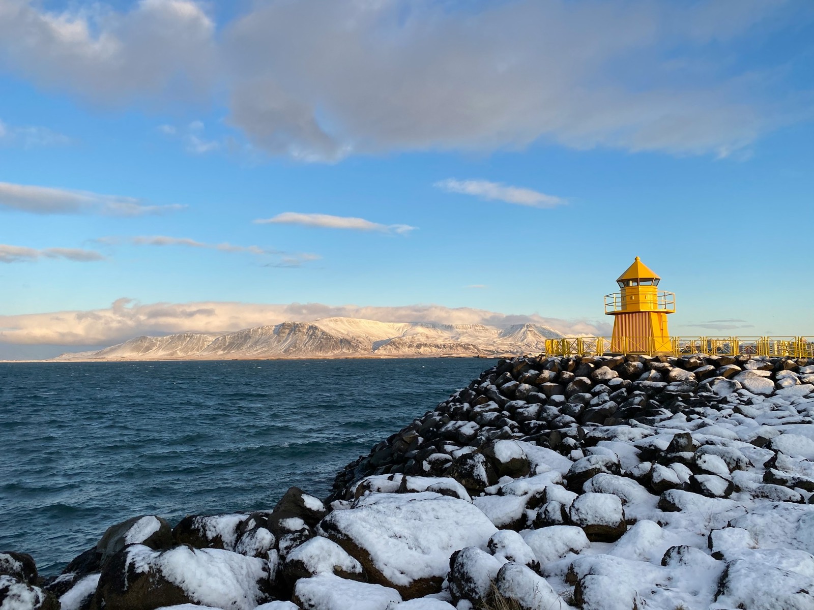 The yellow harbour lighthouse on Ingólfsgarður, Reykjavík, on snow-covered rock with Esja across the bay