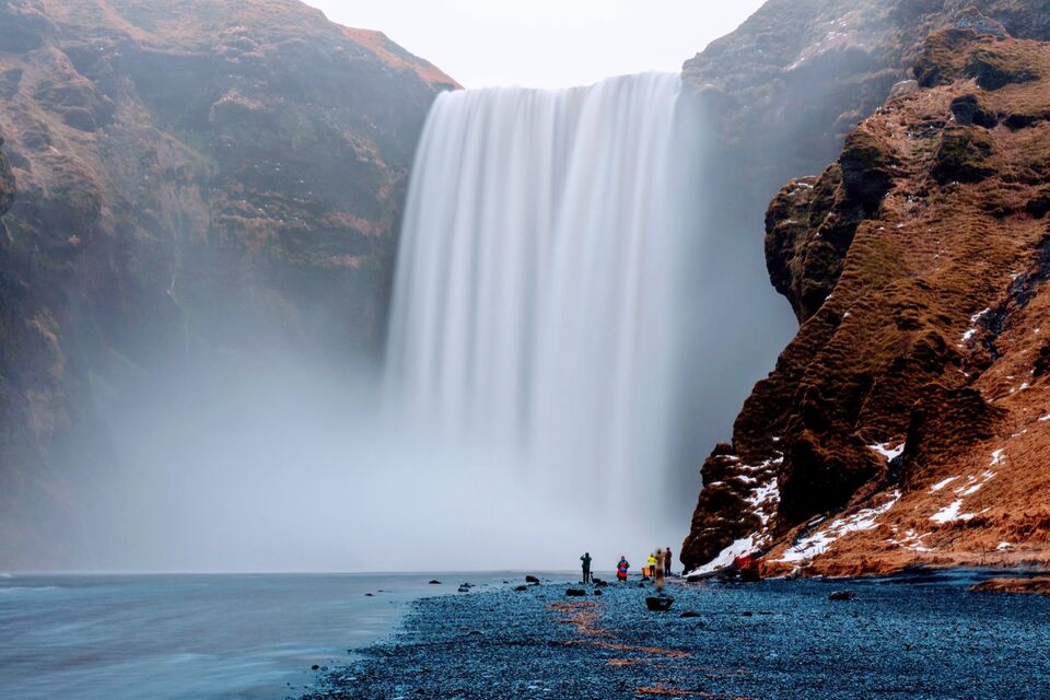 Skógafoss in flat winter light, with photographers on the black gravel at its base for scale