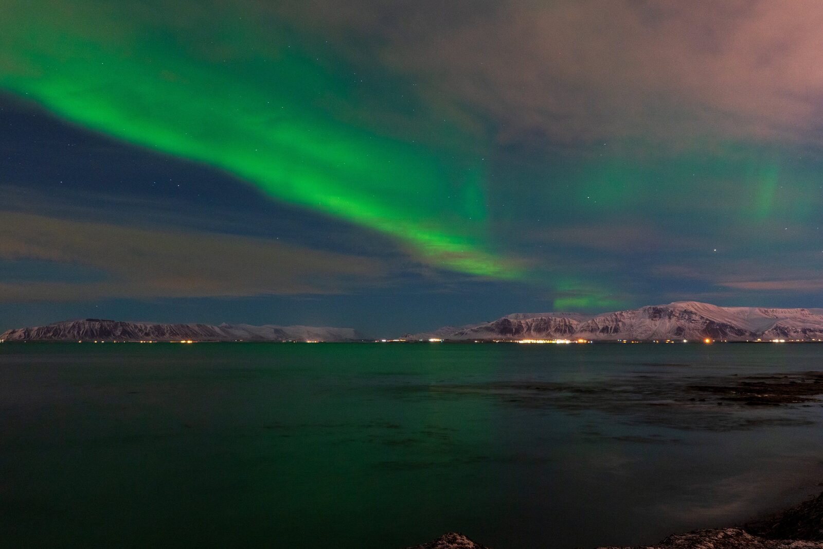 Northern lights arc over Mount Esja across Faxaflói bay