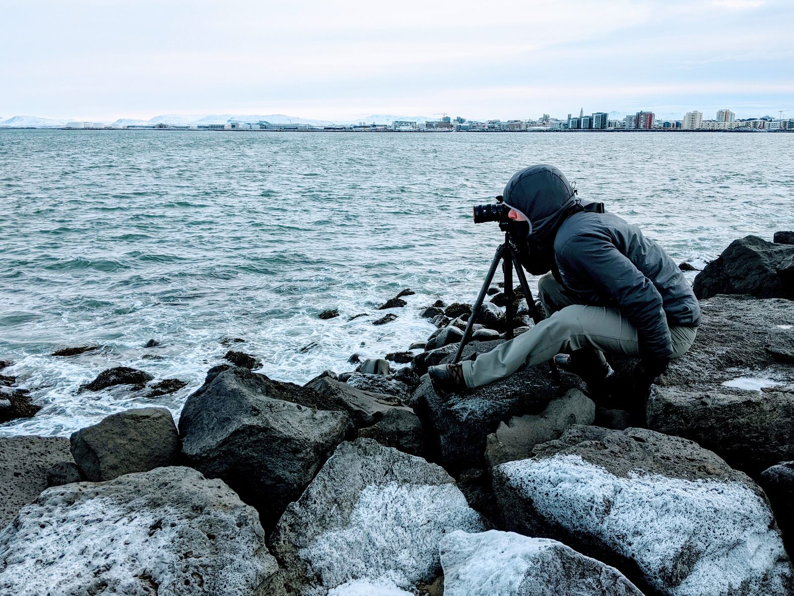 Photographer with tripod on the Reykjavík coastline facing the bay